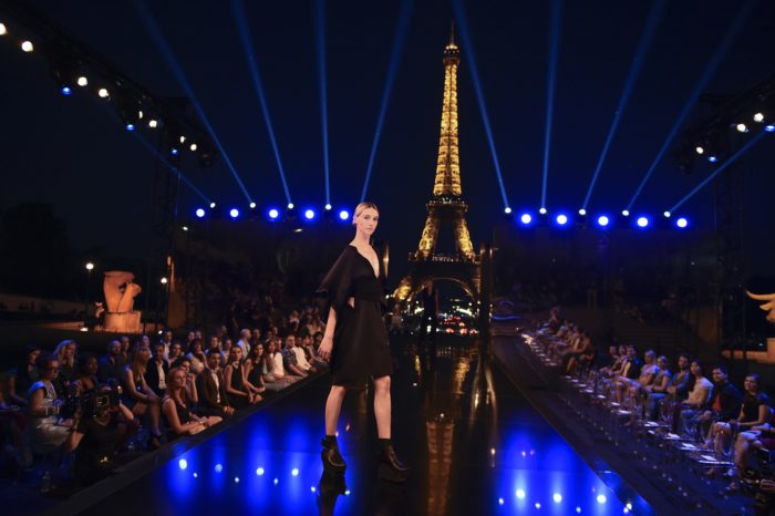 Model in black dress on runway with lit-up Eiffel Tower in background