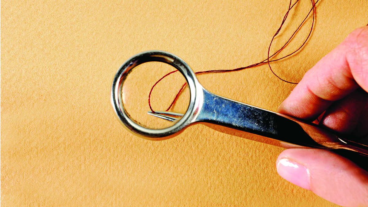 Thread on a needle under a handheld magnifying glass