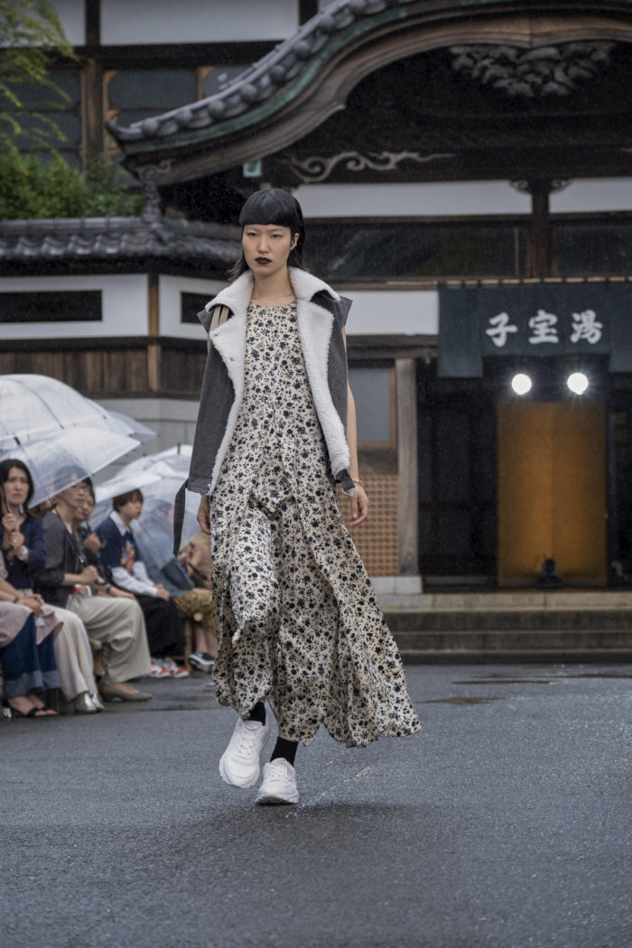 Female model wearing long floral dress with open vest over it