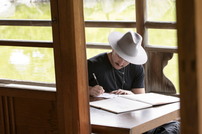 Jonny Cota sitting near a window sketching on paper in Making the Cut Brand Evolution episode