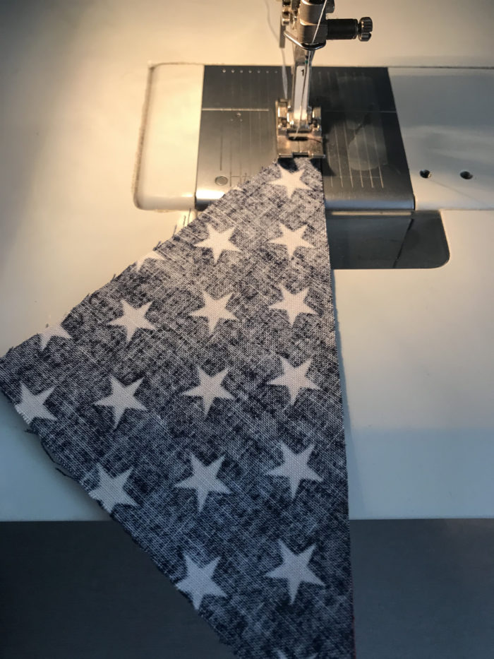 Blue-and-white star fabric triangle being sewn on sewing machine