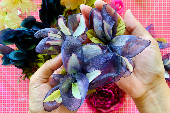 Fabric flowers resembling purple iris blooms held over a pink cutting mat