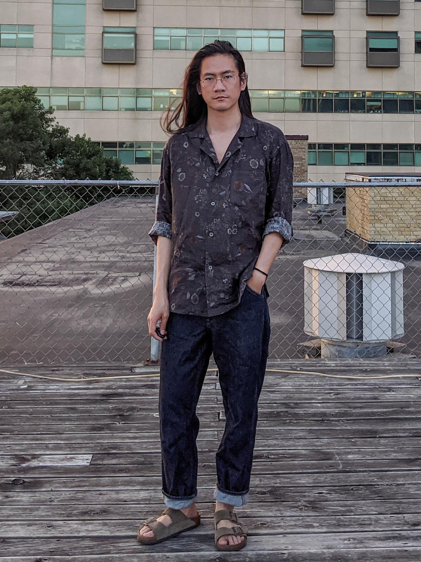 @_Donnyq wears a print shirt and dark jeans, and is photographed on a rooftop.