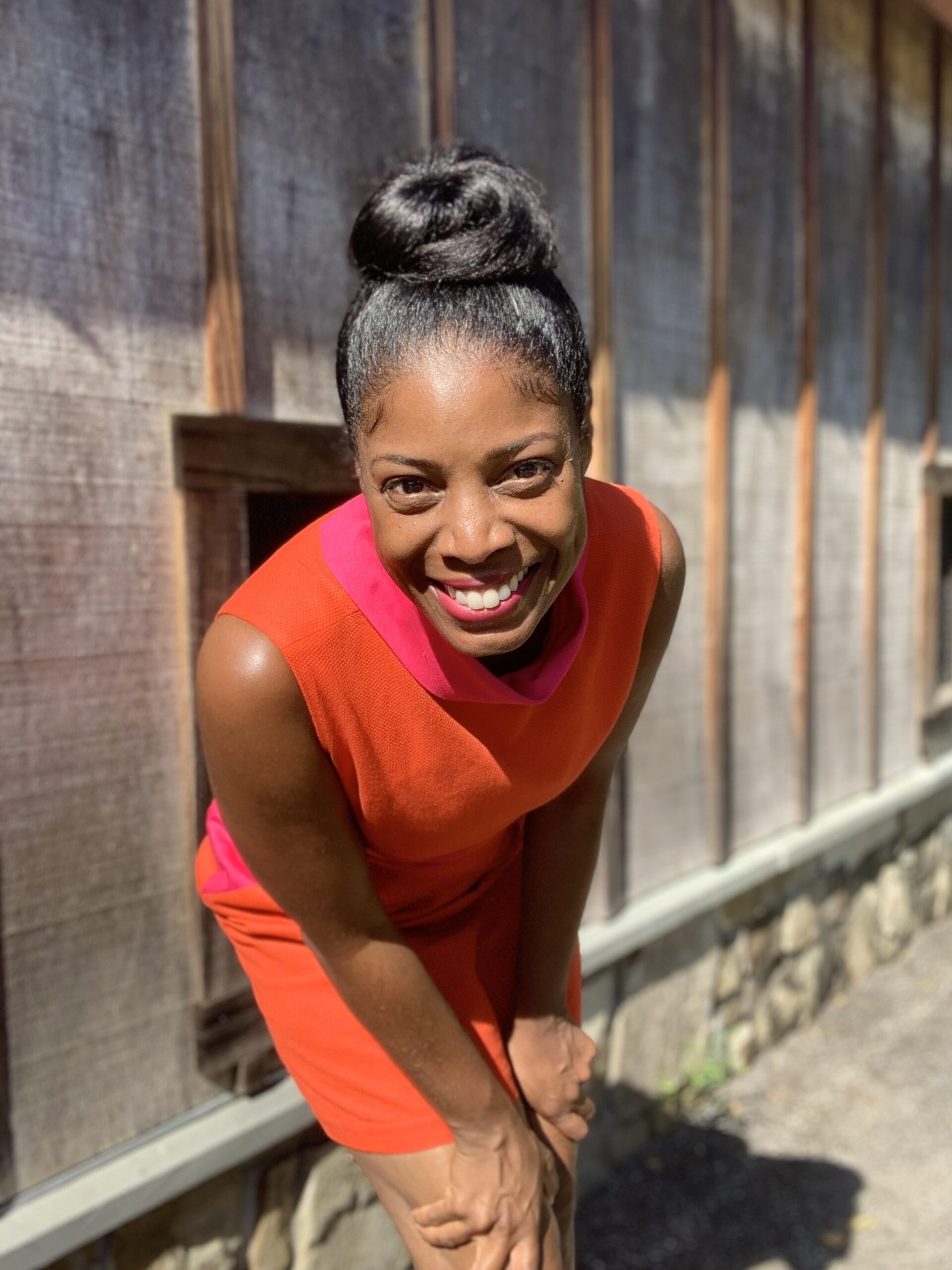 @sewplaysew, a sewing influencer, in an orange and pink dress before a gray fence.