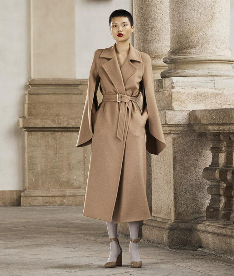 Model wears a long belted brown coat with long, two-piece sleeves.