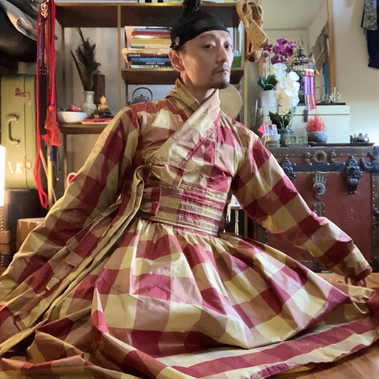 @yang_cheon_shik in plaid hanbok, seated on the floor of an interior space with Asian-inspired decor.