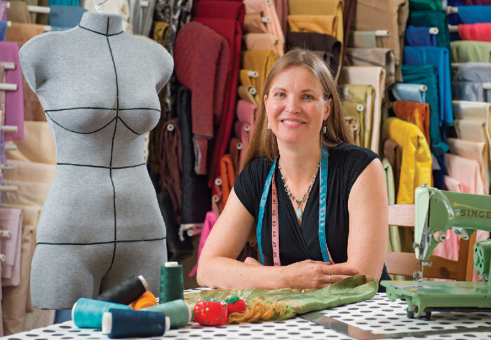 Allison Lince-Bentley sitting in her studio surrounded by textiles and a DittoForm.