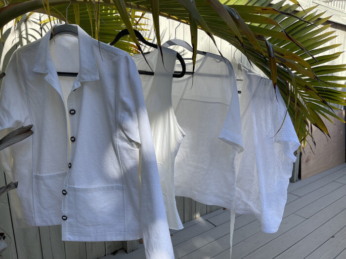 Four white shirts on hangers in a tropical setting