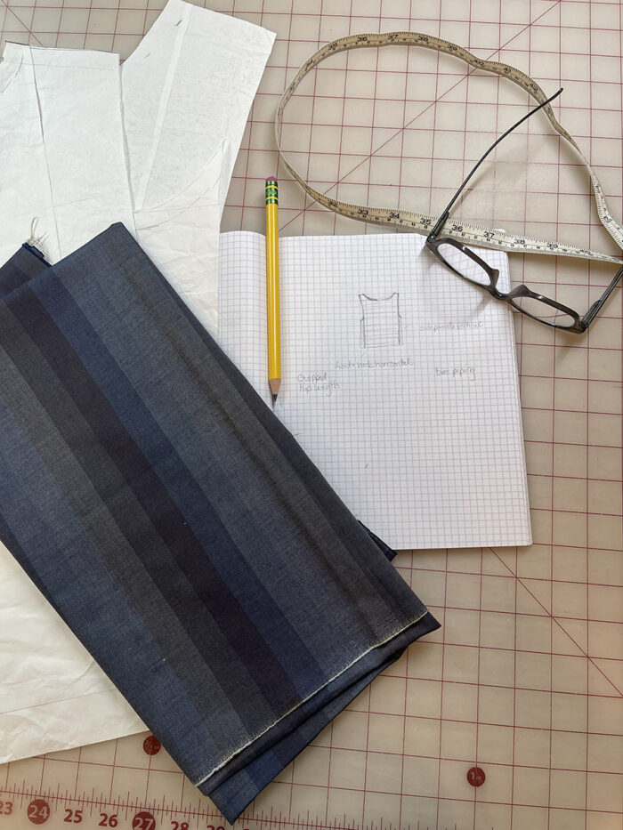 A sketch of a pullover-style top with striped fabric and a tape measure lying on a gridded worksurface