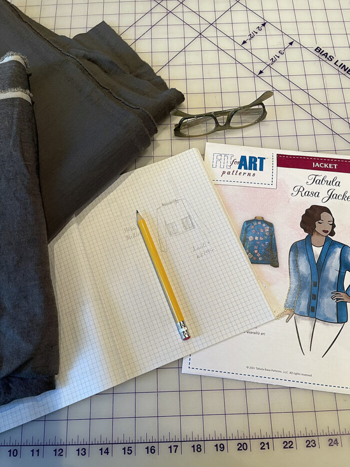 Fabric, eyeglasses, sketch and Fit for Art Patterns Tabula Rasa Jacket pattern envelope on gridded surface