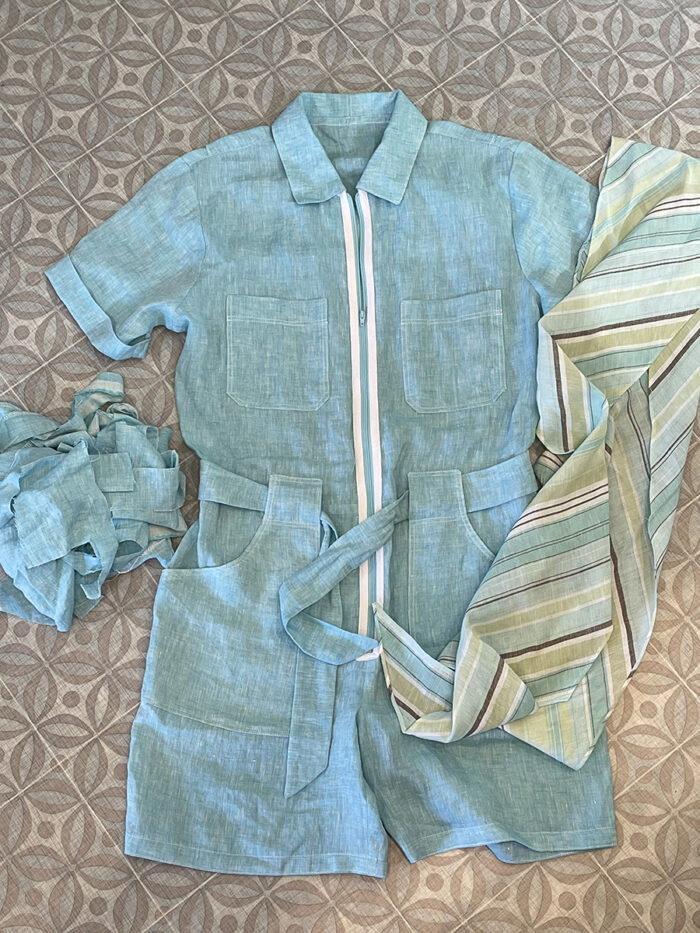 Blue zip-front romper lying on worksurface along with striped fabric and blue fabric scraps