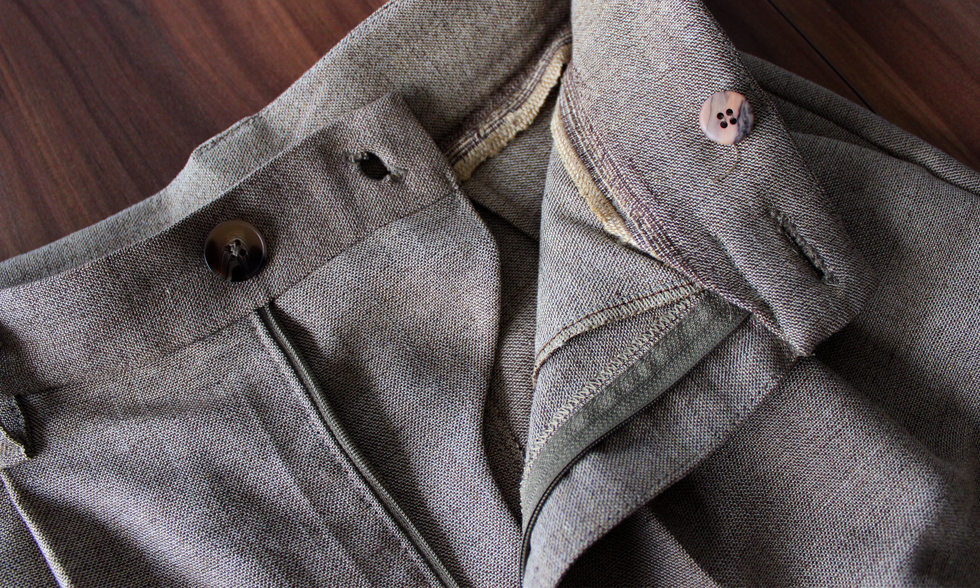 Trouser-making details: Closeup of unzipped tan trousers lying on a table, revealing front fly extension