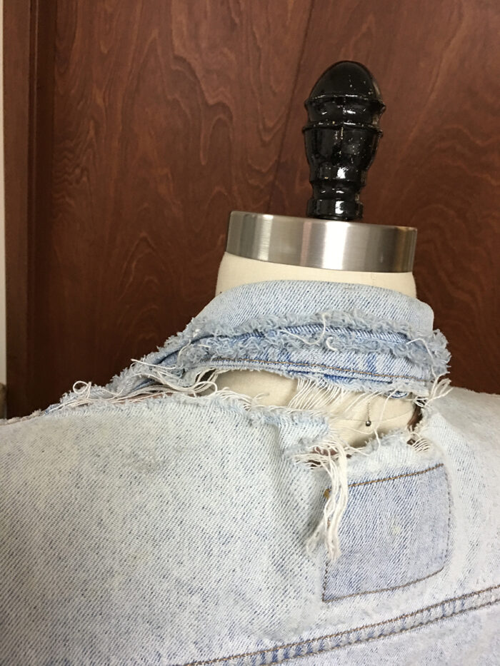 Tattered denim jacket on a dress form, shown from the back